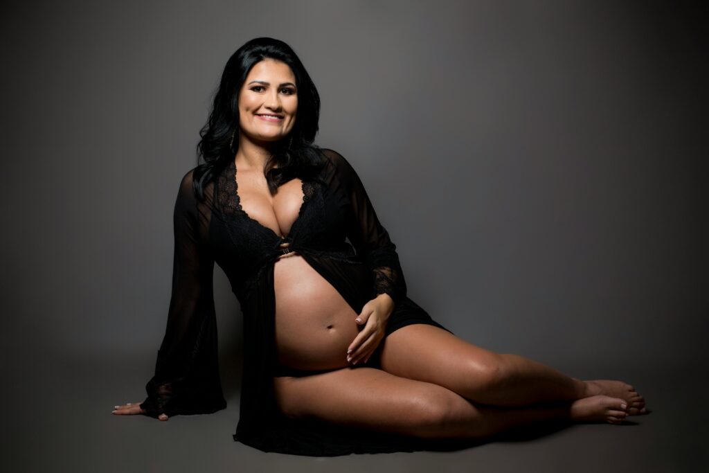 A serene studio portrait of a smiling pregnant woman in elegant maternity wear.